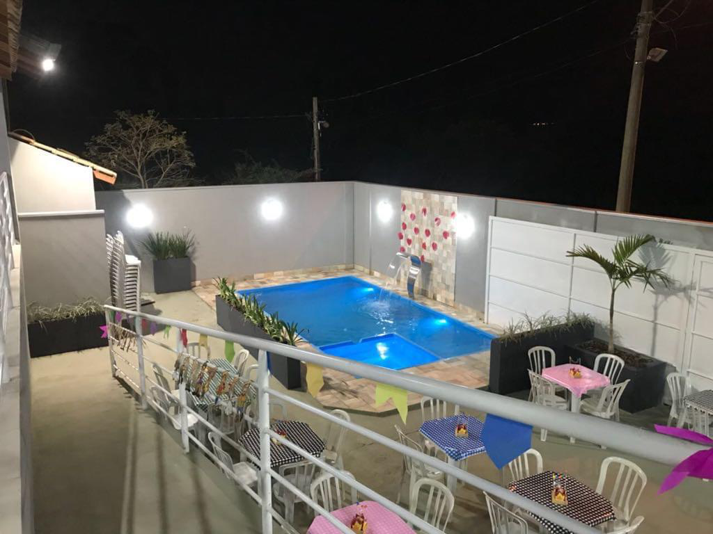 Área de lazer noturna com piscina iluminada, cascata e mesas decoradas