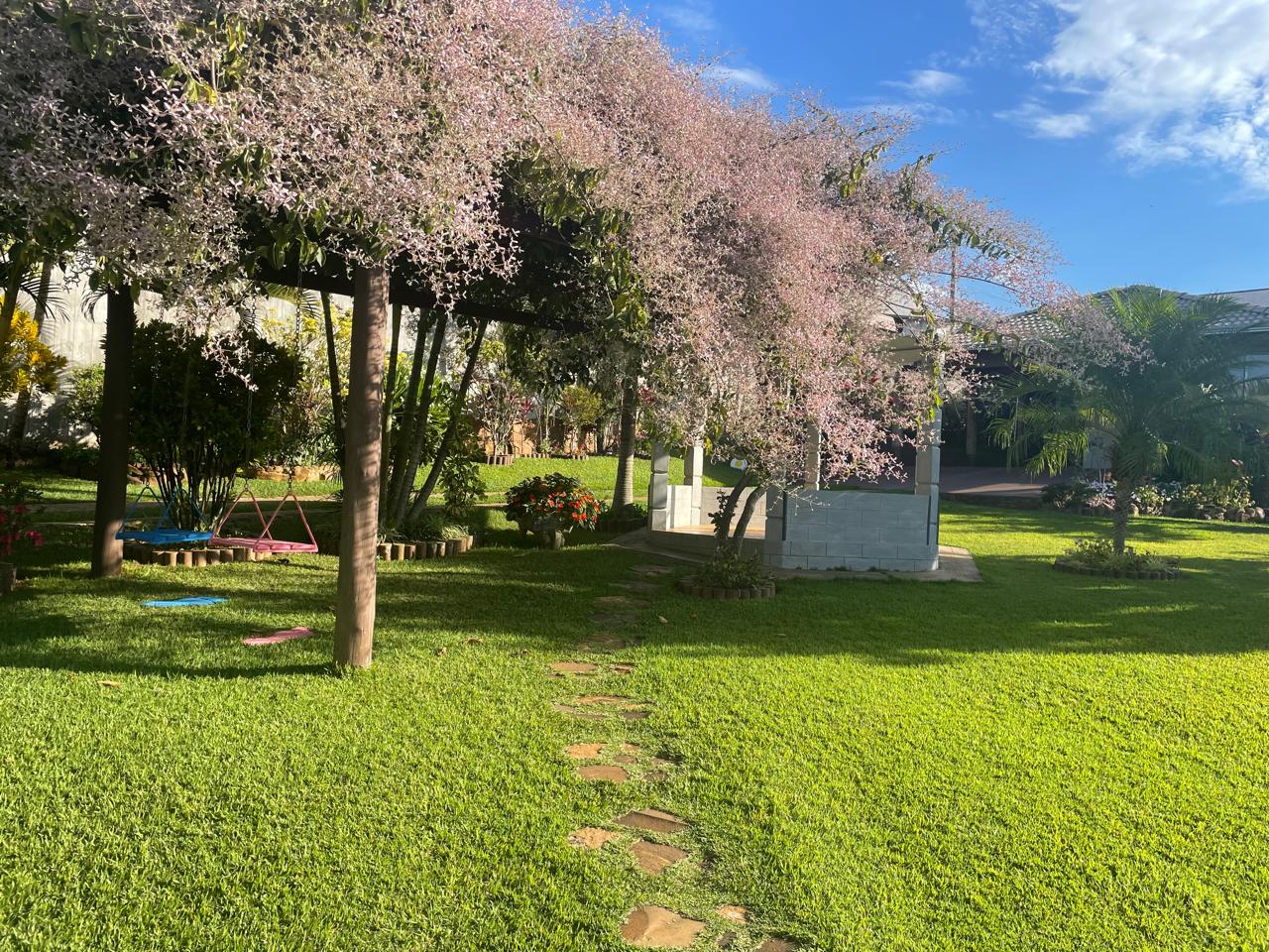 Jardim gramado amplo com caminho de pedras e gazebo florido