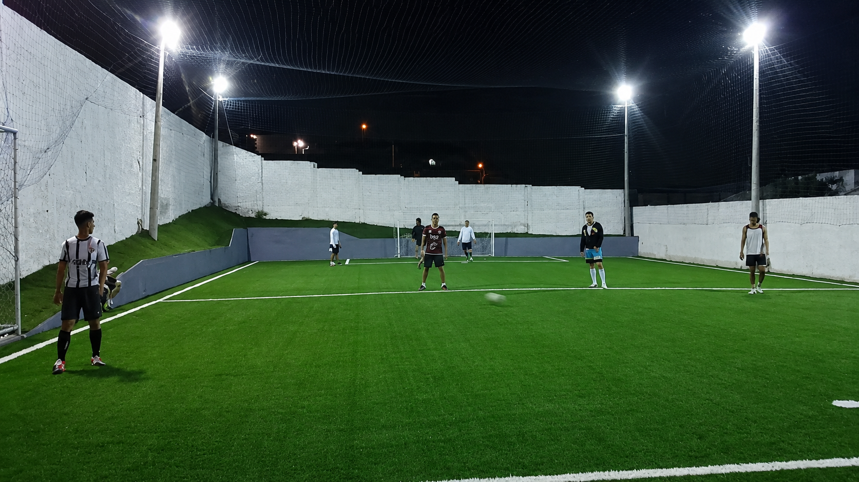 Jogadores em partida no campo de futebol society iluminado à noite